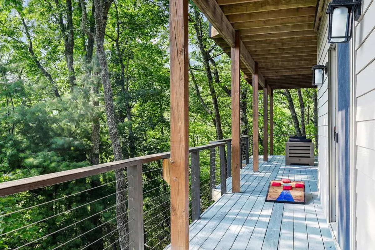 A wooden deck nestled among tall trees, featuring a cozy seating area and an outdoor game set up for play. The deck is surrounded by lush forest, bathed in gentle natural light, offering an inviting space for relaxation and family bonding.