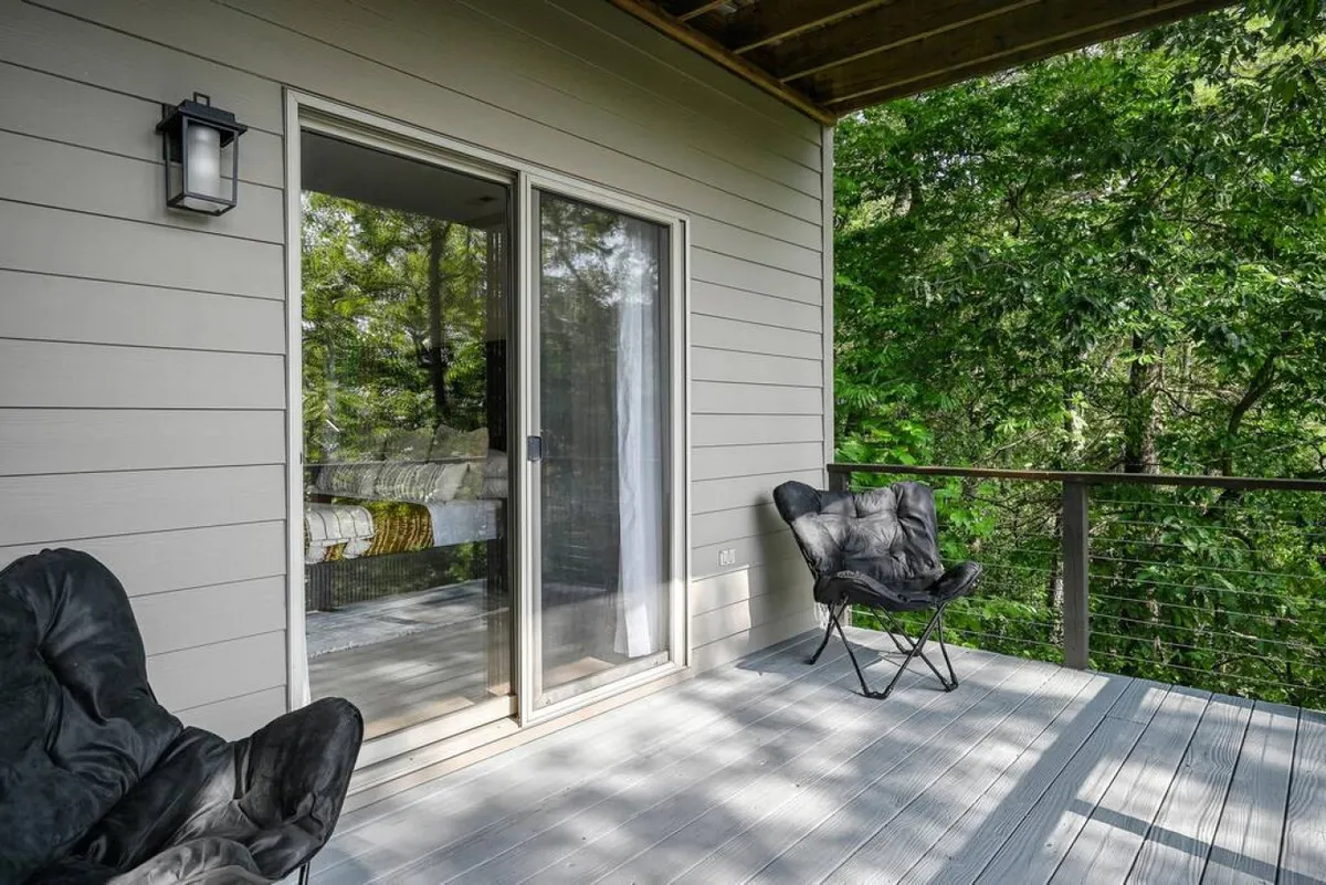 This image shows an inviting outdoor seating area just outside a sliding glass door, surrounded by abundant greenery. The setting is cozy and intimate, designed for enjoying a peaceful coffee break or quiet reading session in nature.