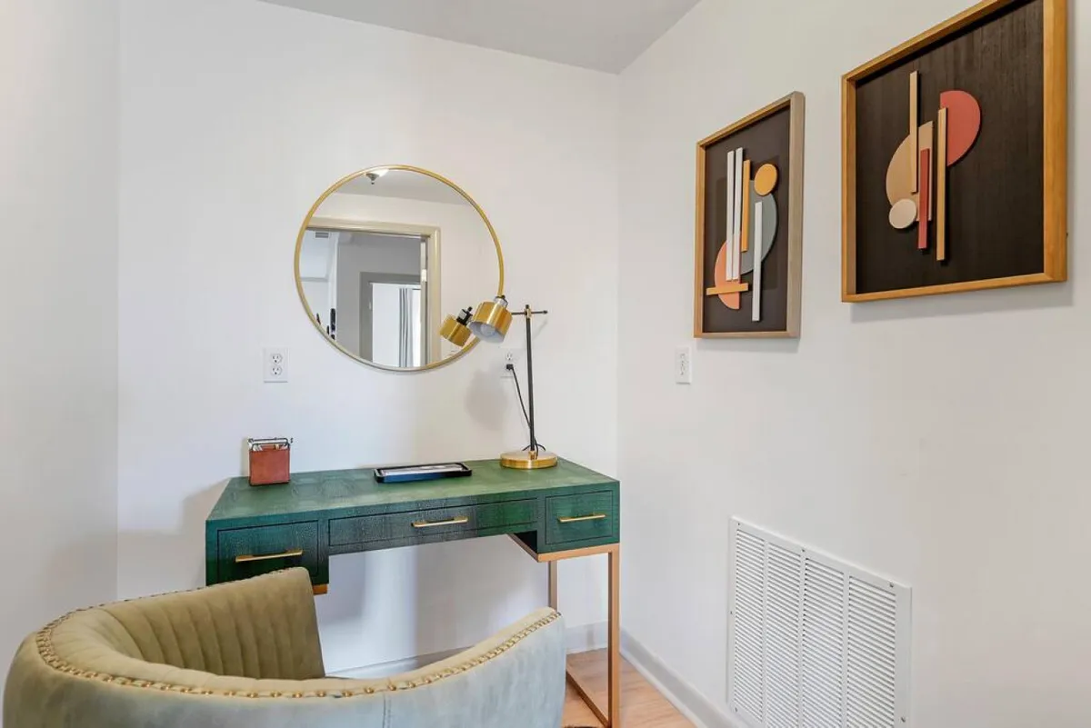 This interior image centers on a green desk with a comfortable chair, round mirror, desk lamp, and inspiring wall art. The space is calm and inviting, designed for productivity and creative work.