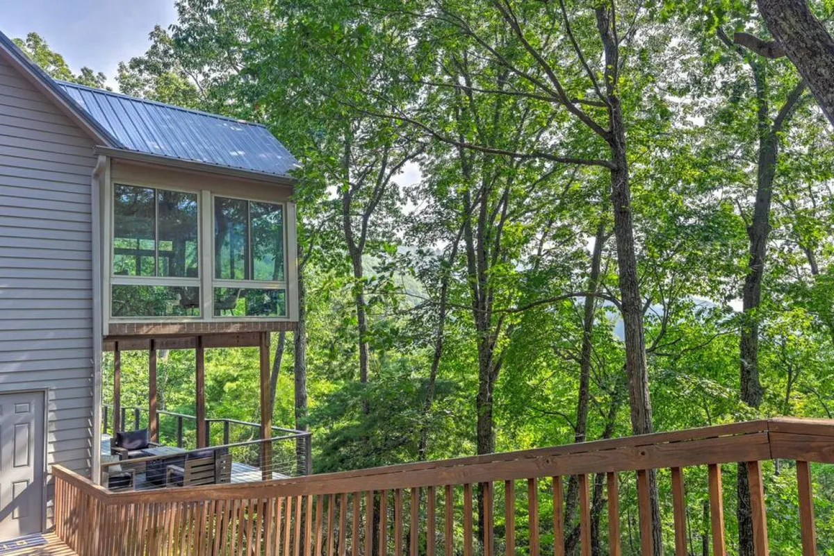 An inviting deck area bordered by trees, with large glass windows connecting the exterior to the interior spaces. The deck offers plenty of room for socializing outdoors, whether it's hosting a BBQ or simply relaxing while taking in the mountain views through the trees.