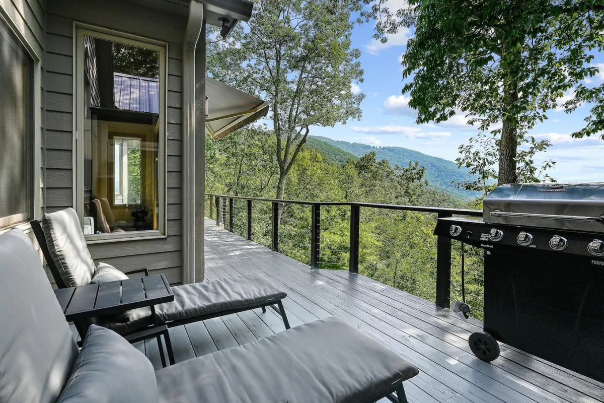 This exterior shot showcases a wooden deck with comfortable chairs and a propane grill, set against a backdrop of sweeping mountain views. The deck is ideal for al fresco dining and BBQ nights, with ample room to relax and take in the scenery.